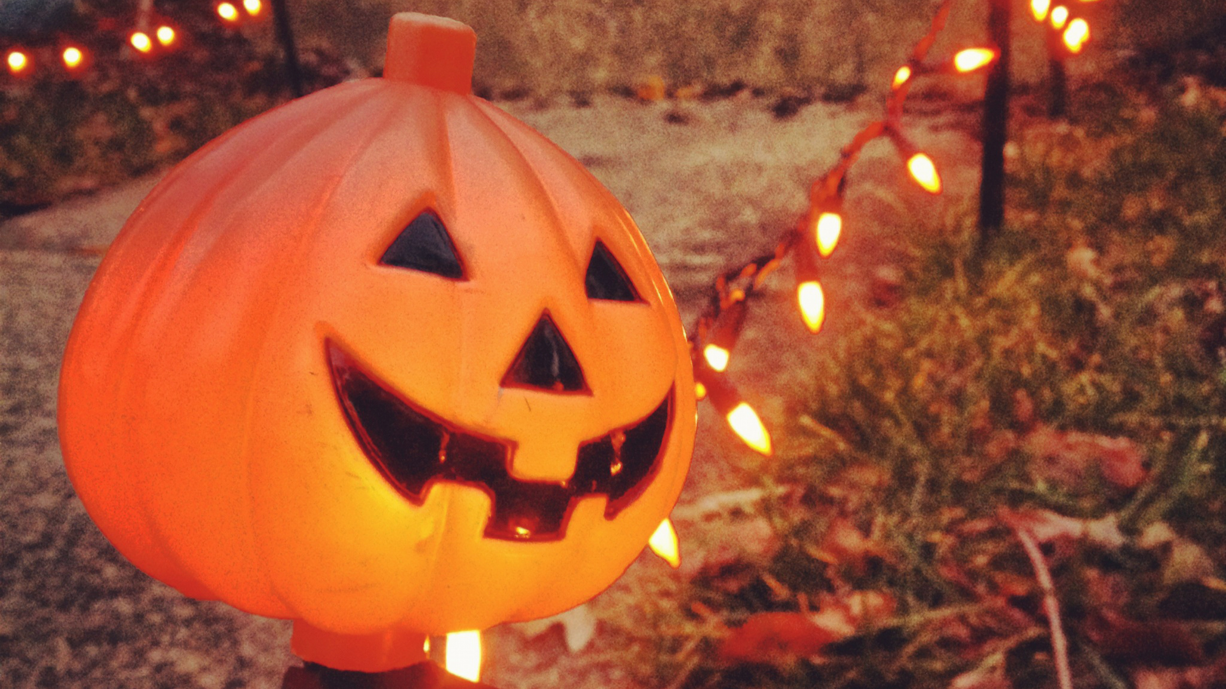 pumpkin garden stake at dusk with string lights in the background