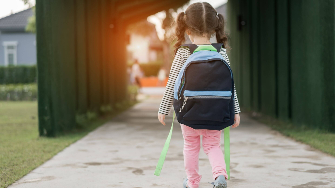 little girl in school playground with blue and green backpack