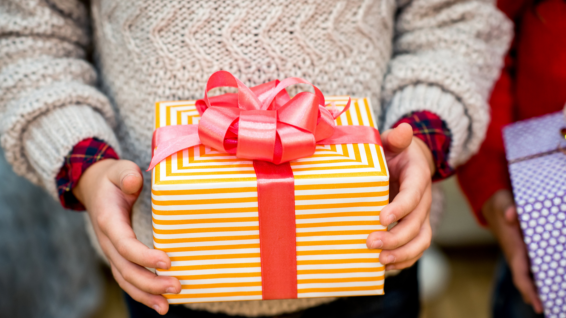 little boy holding a gift wrapped in striped paper with a large red bow on top