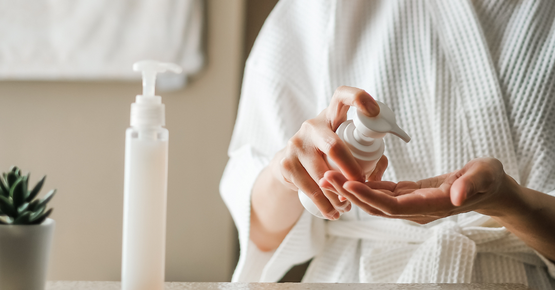 person wearing white waffle robe in bathroom with skincare bottles on counter beside aloe vera plant