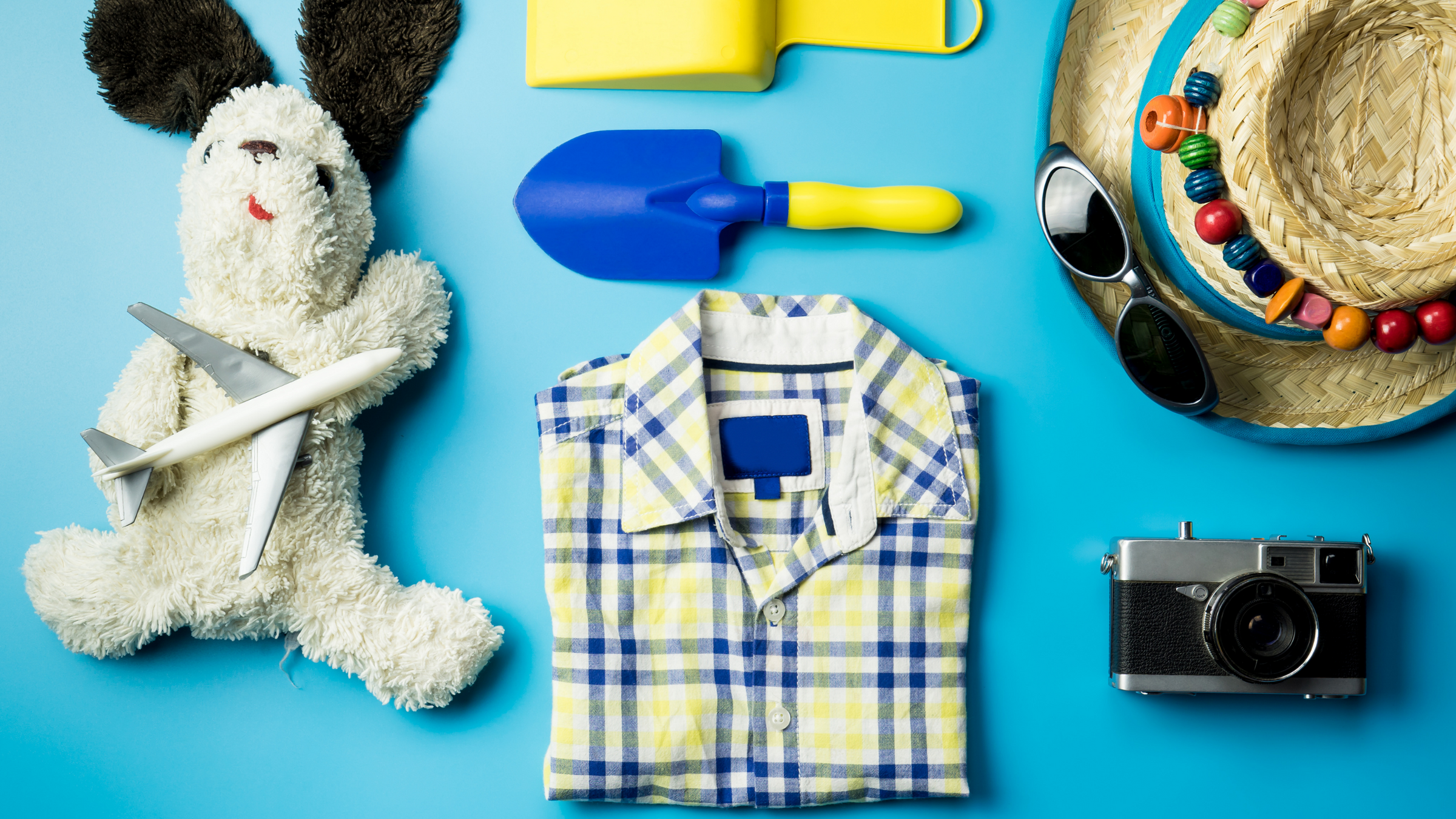 blue background with boys shirt, summer hat, sunglasses and teddy bear