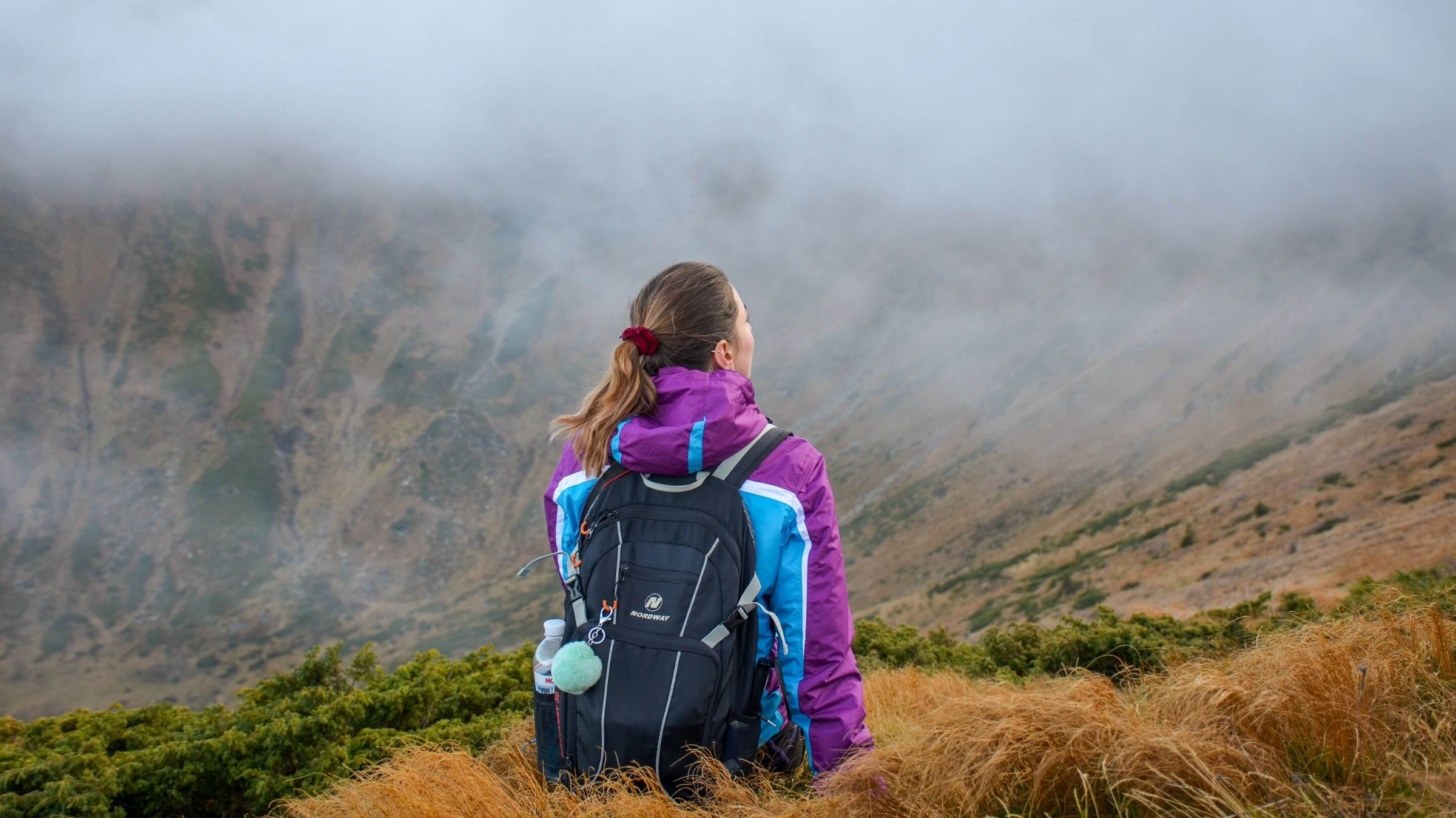 lady wearing hiking backpack at the top of a misty mountain