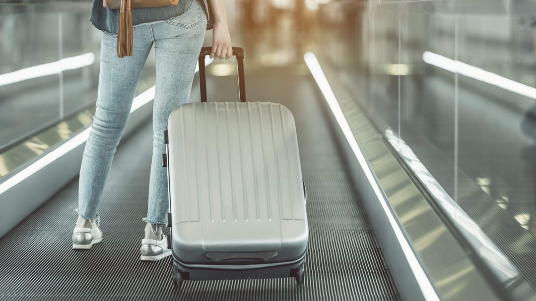 person at airport with silver hard shell suitcase