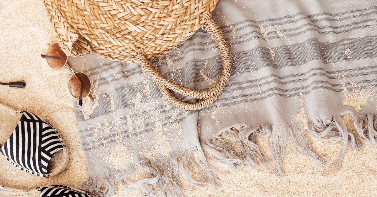 beach bag on beach towel beside sunglasses and sandals at the beach