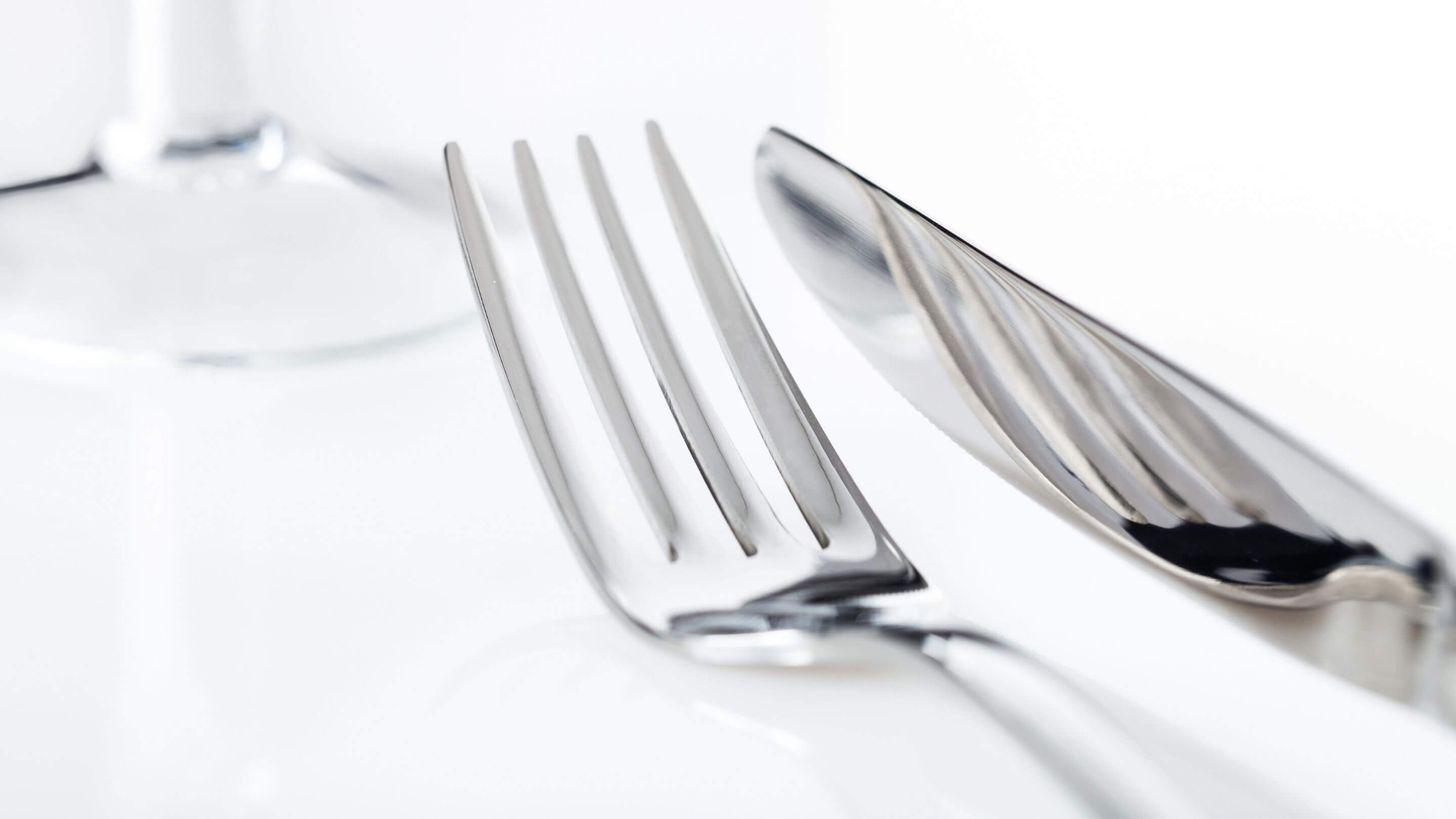 silver stainless steel fork and knife on white counter with wine glass in the background