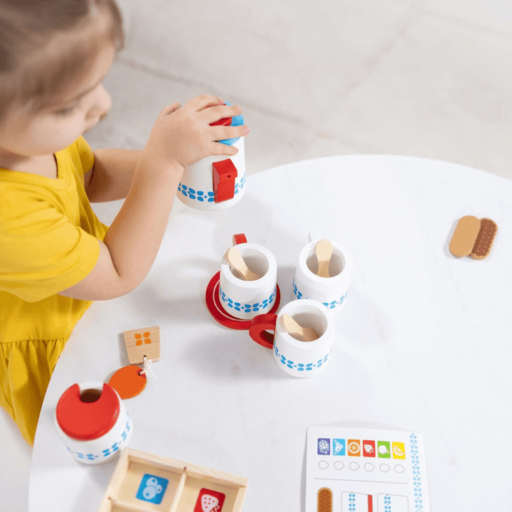 little girl uses teapot to pour tea into mugs with wooden spoons inside ready to stir