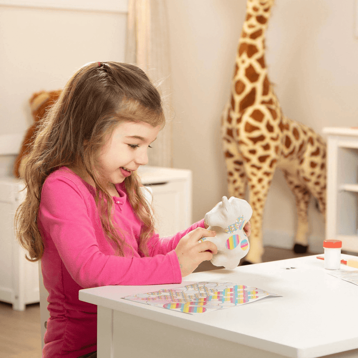 little girl smiles as she adds stickers to the unicorn at home