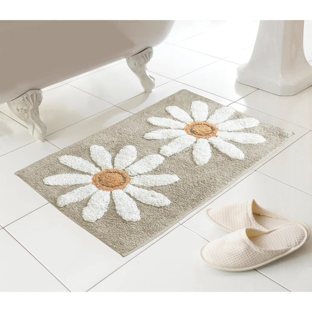 Natural colour bath mat with 2 large white daisies pattern on a tiled floor next to a bath and slippers