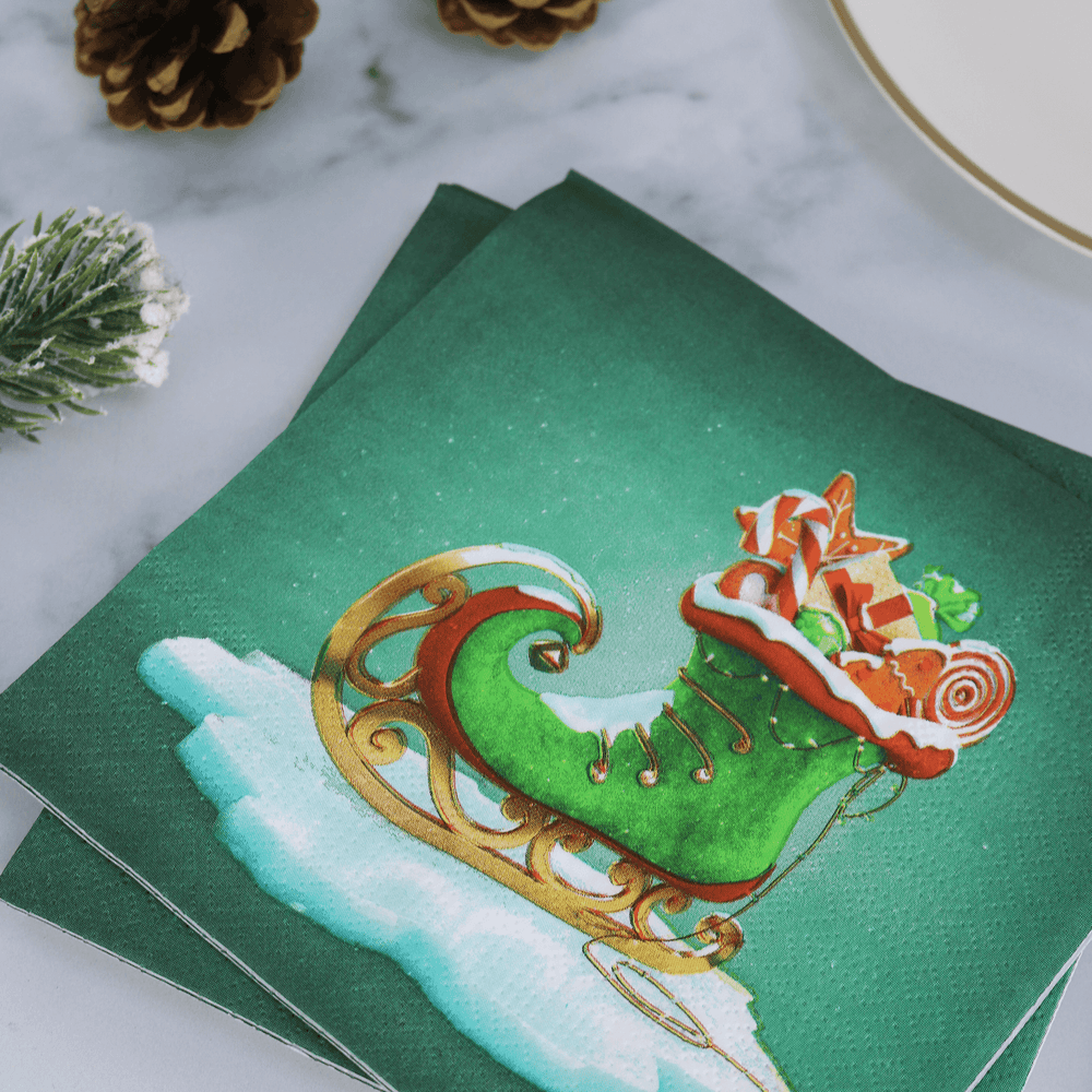 green elf boot santa sleigh napkin on christmas table beside plate and pine cone decorations