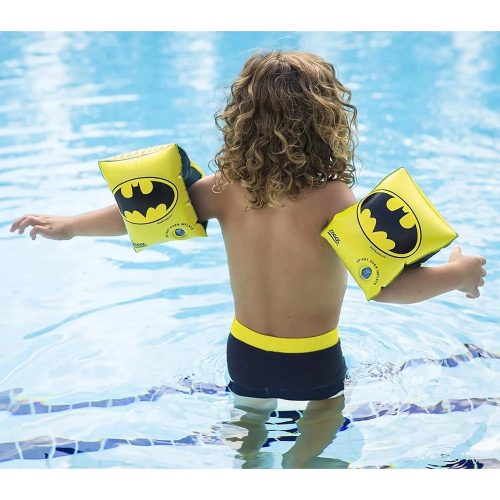 Child standing in a swimming pool with Batman logo swim bands on