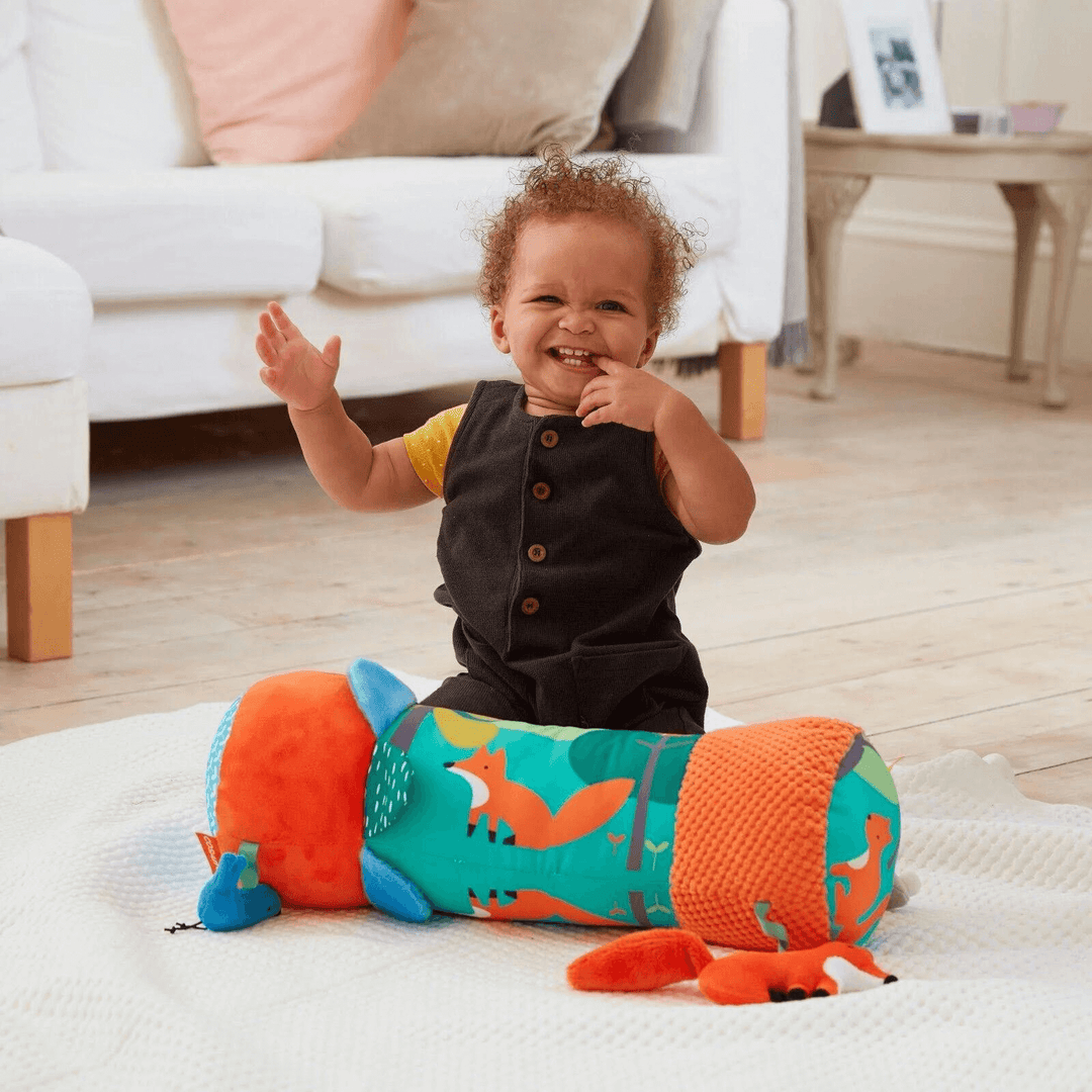 little baby in living room smiling and playing with orange tummy time roller.