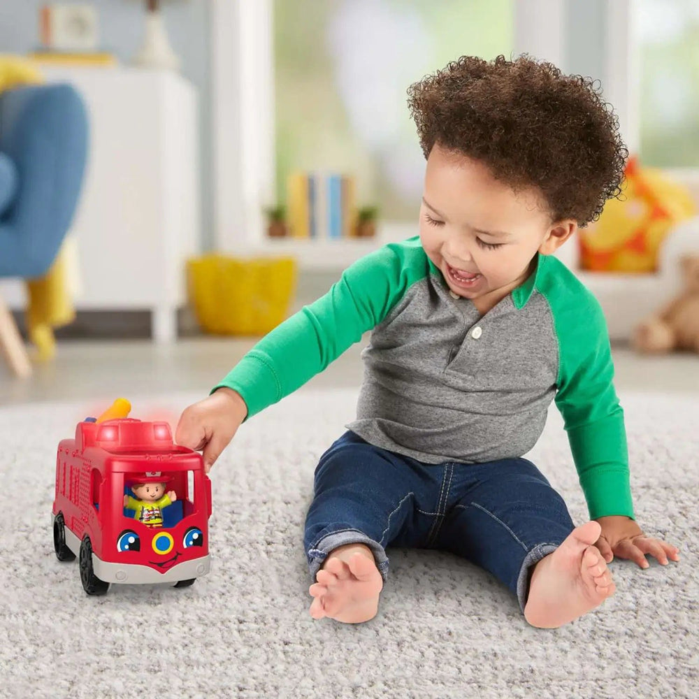 Toddler sitting on a carpet playing with a Little People Fire Engine that lights up and make sounds