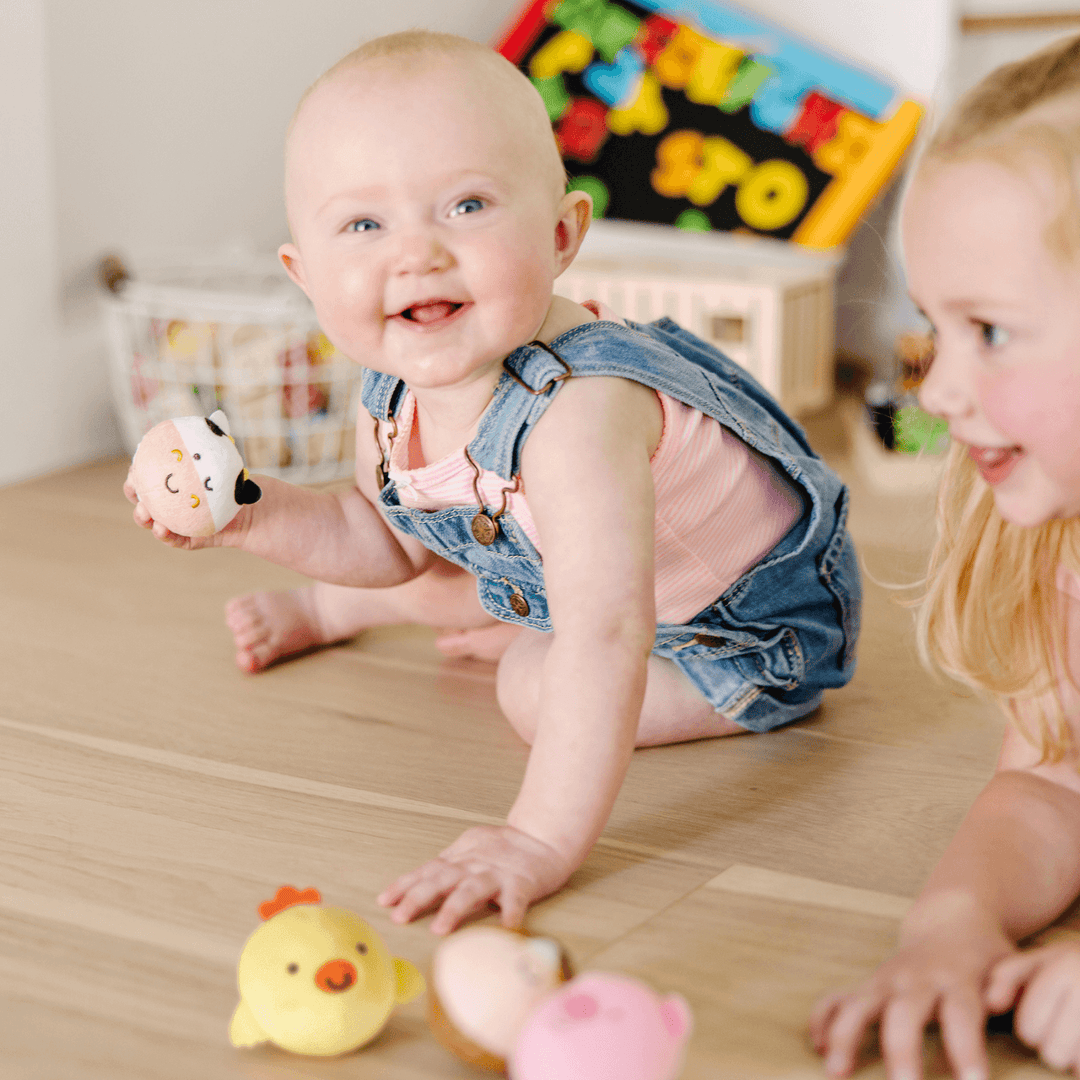 baby smiles and holds cow farm friend rollable in hands