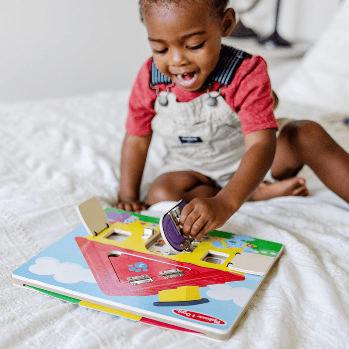 young boy opens wooden door on activity board to reveal storytelling fun, surprised expression