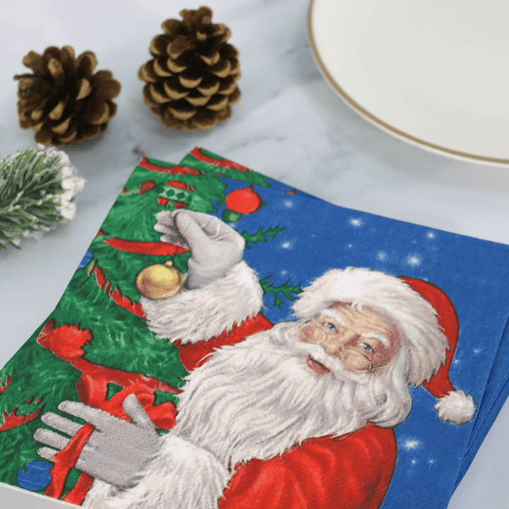 santa claus and christmas tree paper napkins on table beside plate and pine cone decorations