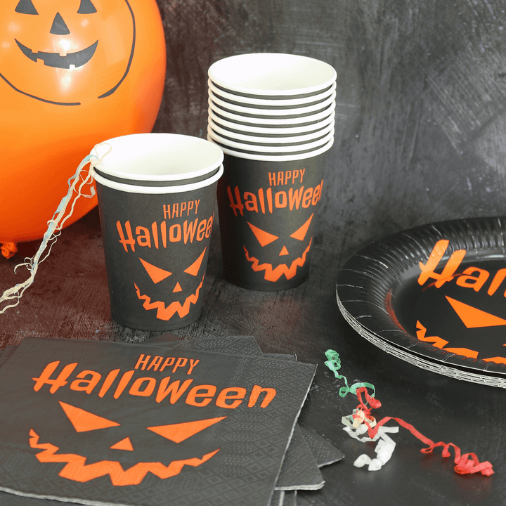 black halloween table set up featuring orange and black happy halloween paper cups, paper napkins and paper plates with orange pumpkin balloon in the background