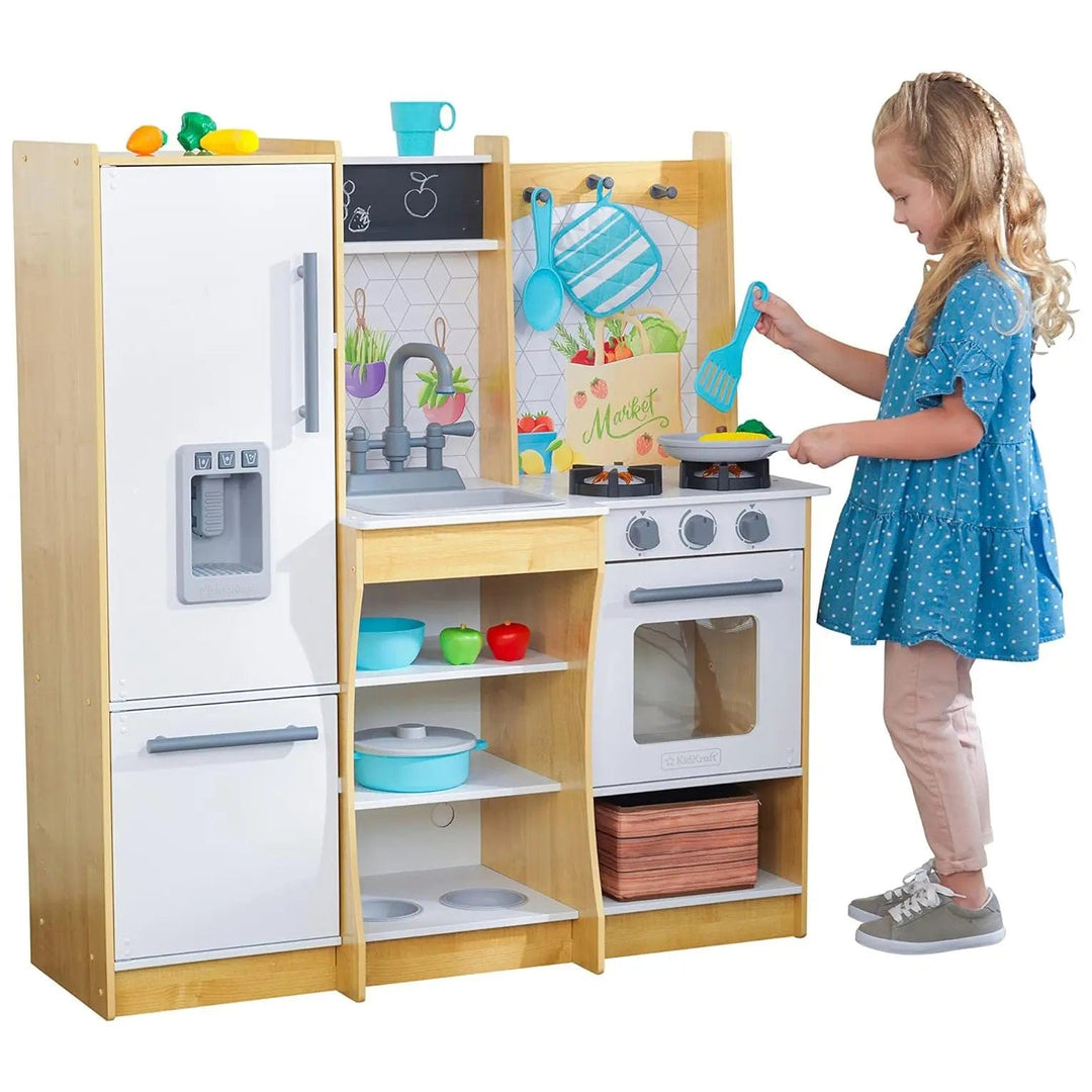 Girl playing with a toy wooden kitchen with cooker, fridge, shelves, oven and lots of accessories