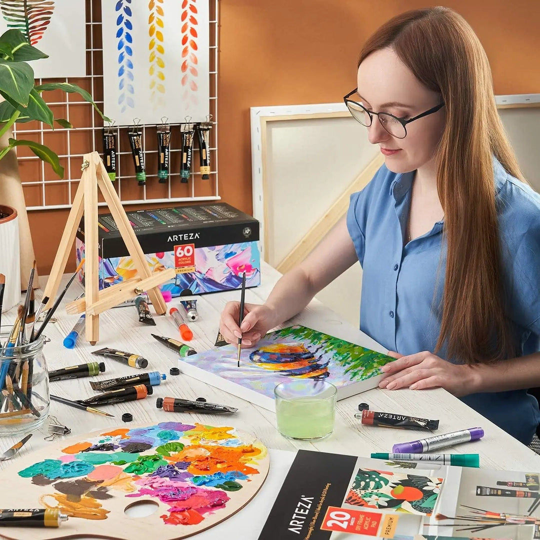 Artist at a desk, creating work with Arteza acrylic paints, paper and palette