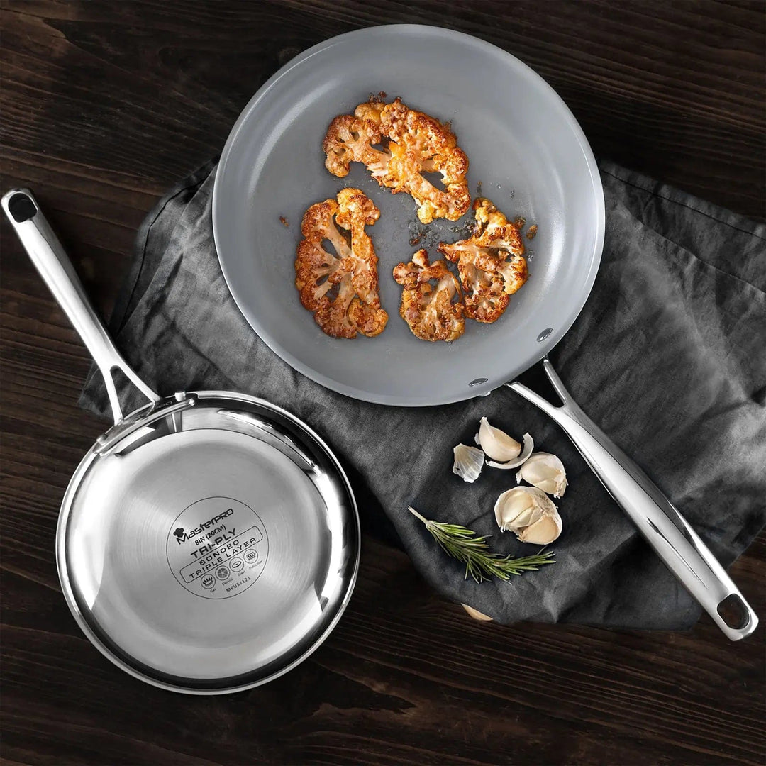 Overhead view of 2 grey and silver frying pans, one with fried cauliflower slices, the other turned over to show the base