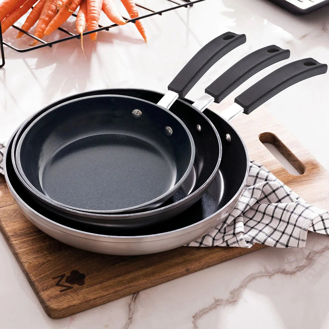 3 frying pans nested together on a kitchen chopping board with tea towel and carrots