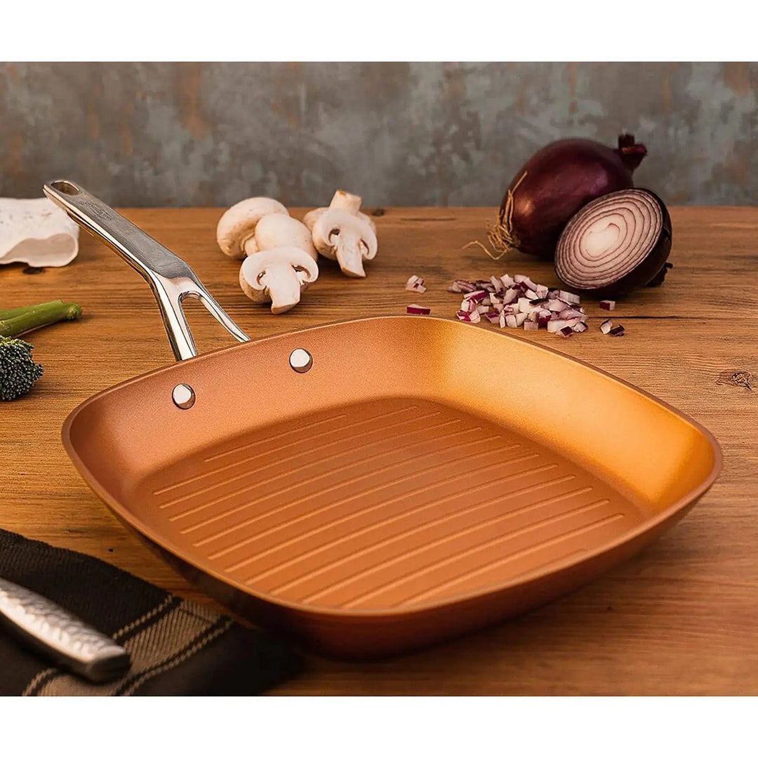 Copper grill pan with stainless steel handle on a wooden table with mushrooms, onion and brocolli