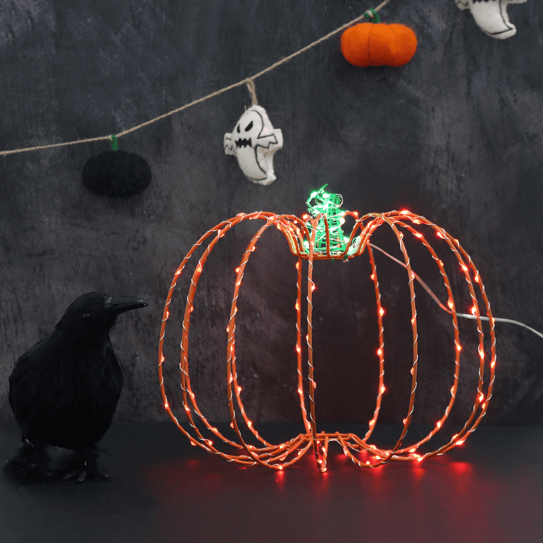 Pumpkin LED decoration featuring LED lights in purple and green colours sitting on black table beside crow decoration