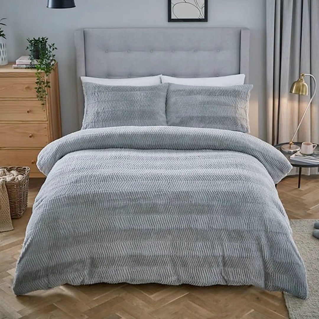 Double bed with grey faux fur bedding with chevron style pattern, silver headboard and parquet floor