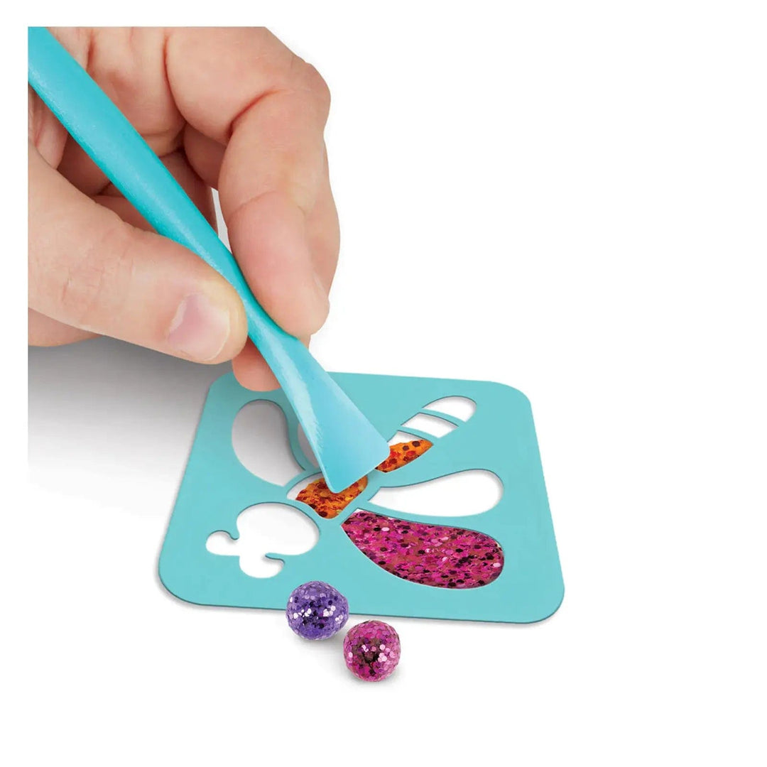 Hand holding a modelling tool to press in a Glitter Dot into a butterfly stencil