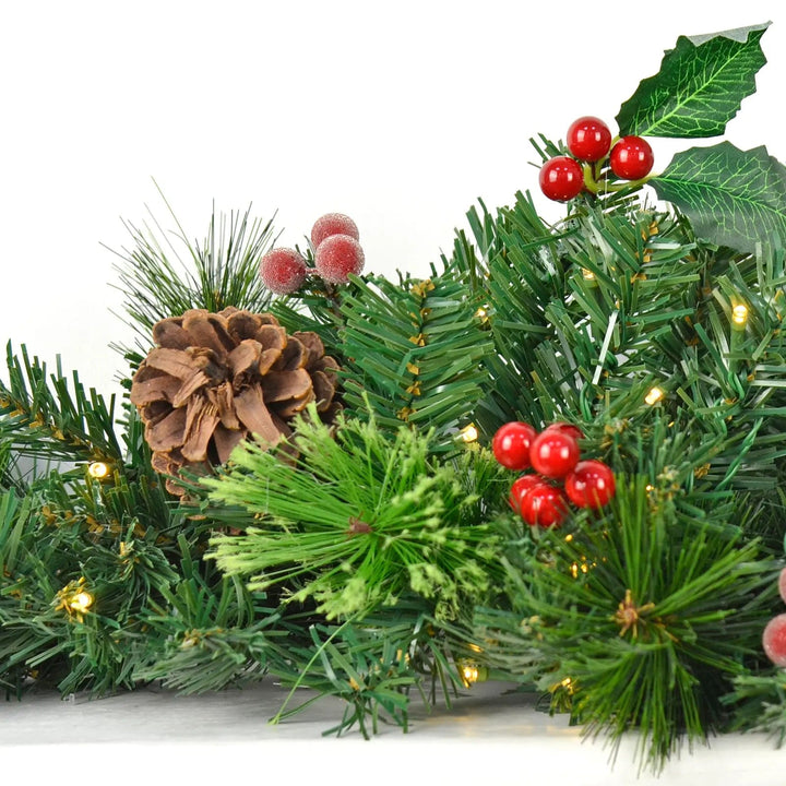 Close up of a Christmas swag decoration with mixed artificial pine and holly branches with red berries and white LED lights