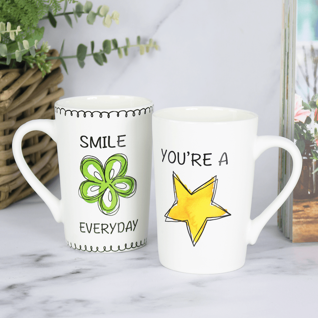 two porcelain mugs on marble worktop surface beside cook book featuring bold colour prints and slogans