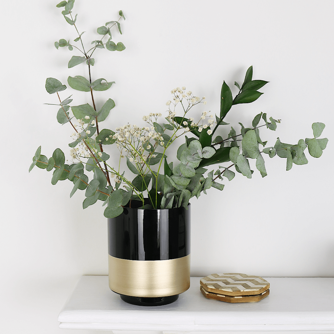 black and gold vase filled with eucalyptus flowers on fireplace mantel ledge beside wooden coaster