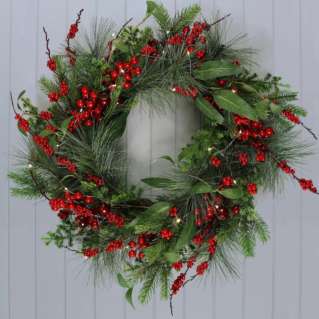 Christmas wreath with fairy lights, red berries and mixed green foliage hanging on a panelled wall