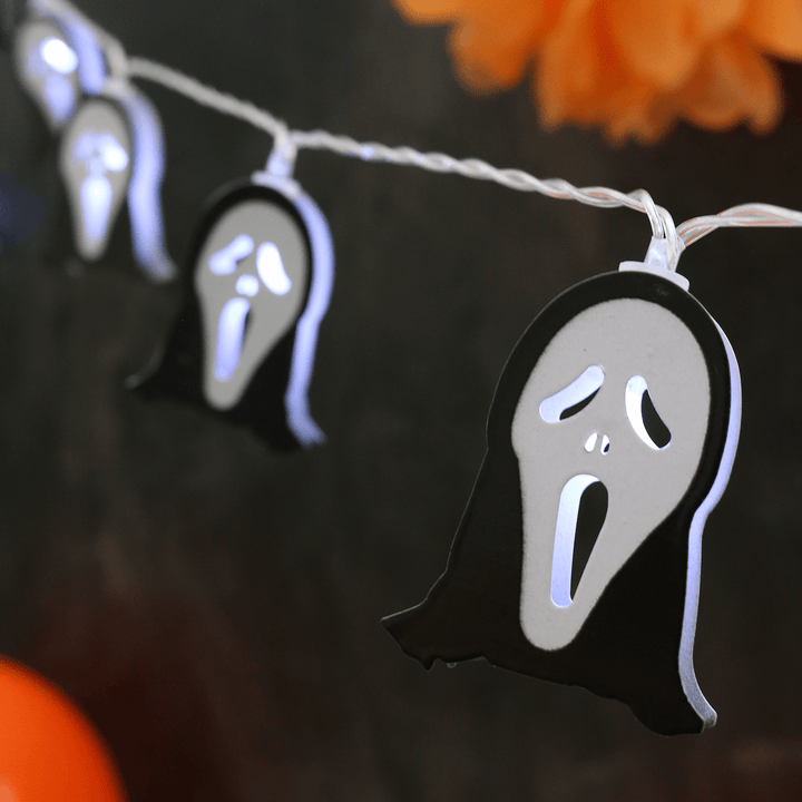 metal ghost face string lights with bright white LED light on black background with orange decorations in the background