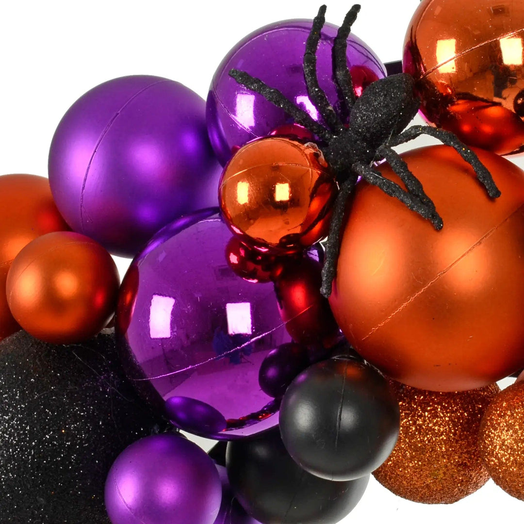 Black glitter spider, orange and purple baubles on a Halloween wreath