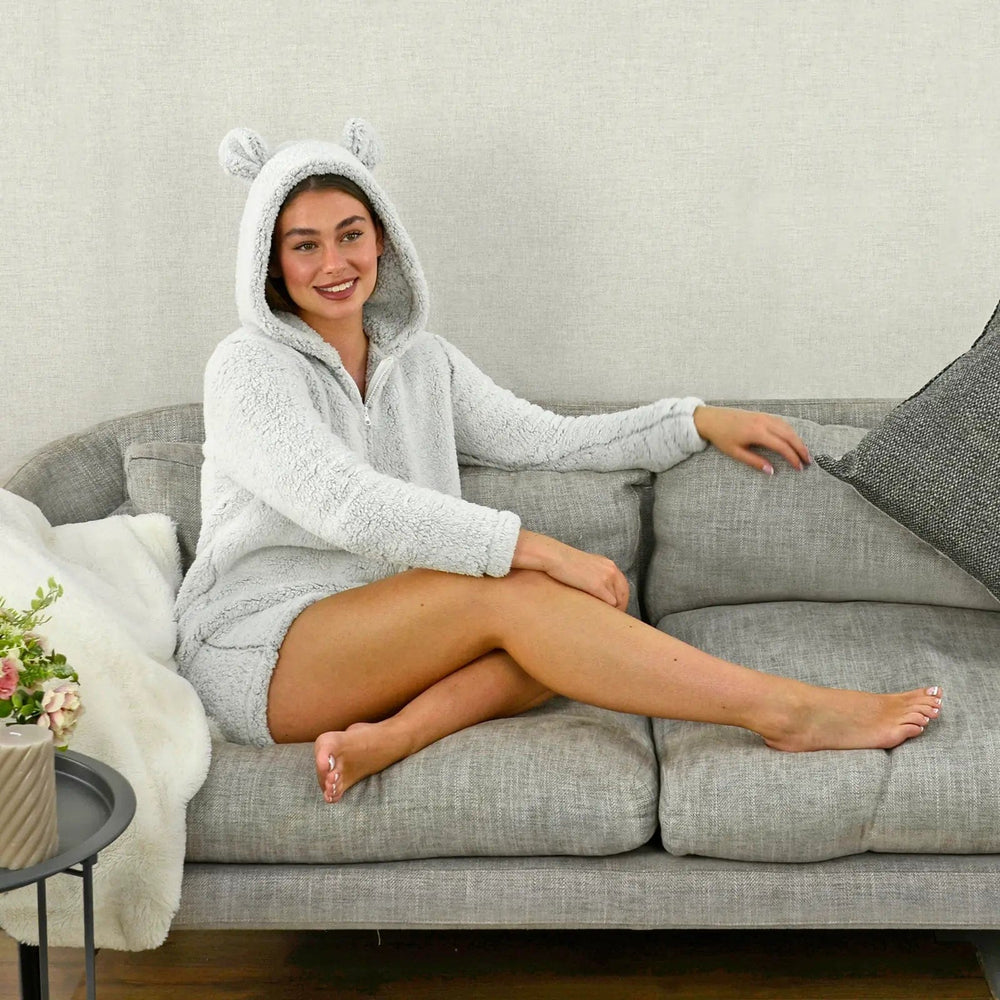 Young lady wearing a pale grey fleece hooded romper suit, sitting on a grey sofa