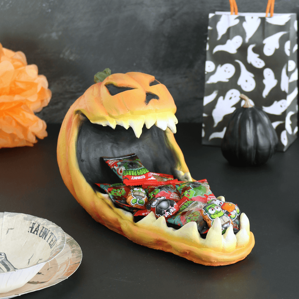 orange latex pumpkin tray on black table holding a variety of halloween gummy sweets with black pumpkin and ghost treat bag in the background