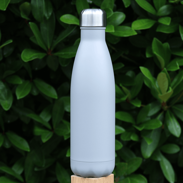 grey coloured stainless steel vaccum bottle with silver screw top lid on fence post in front of evergreen tree outdoors