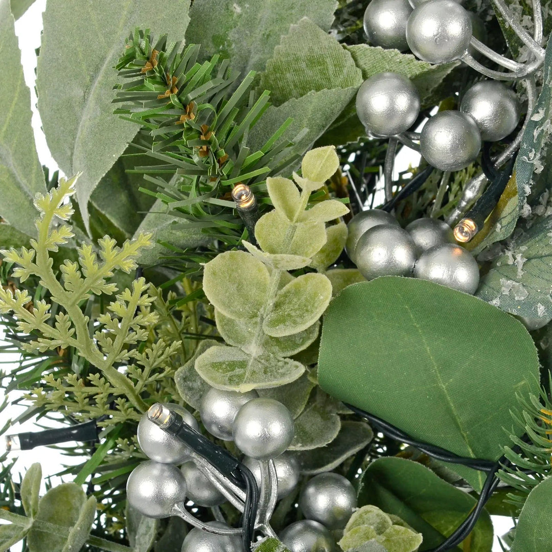 Close up of LED lights, silver berries and green foliage on a Christmas wreath