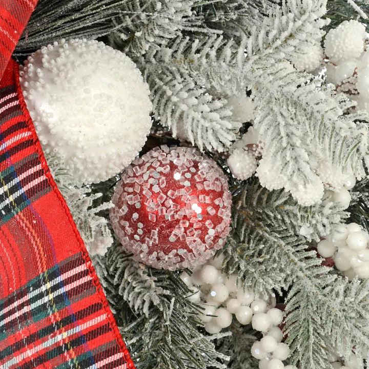 Close up of red tartan ribbon, white and red baubles and frosted pine branches