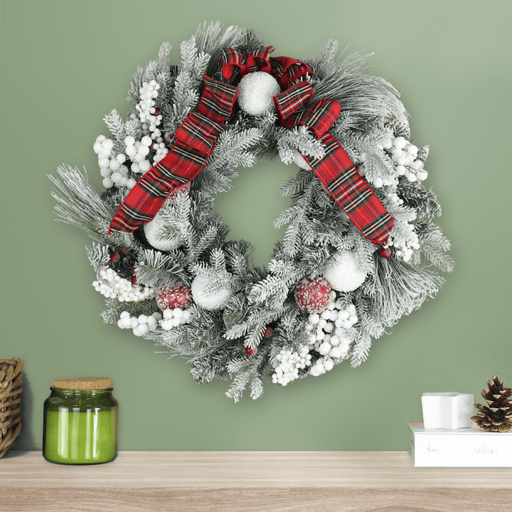 red and white tartan wreath on green wall above fireplace mantel
