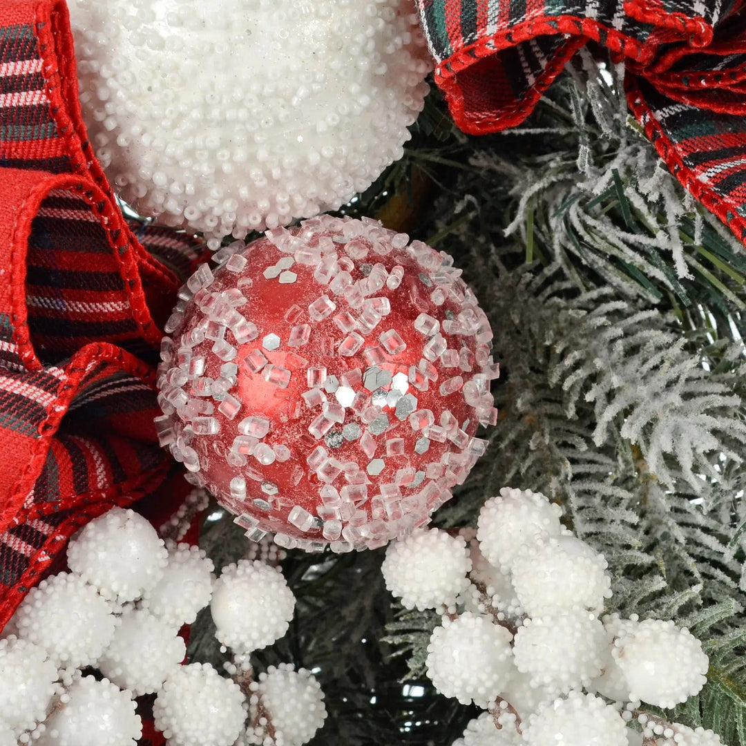 Close up of red and white frosted baubles, snow berries and green pine branches