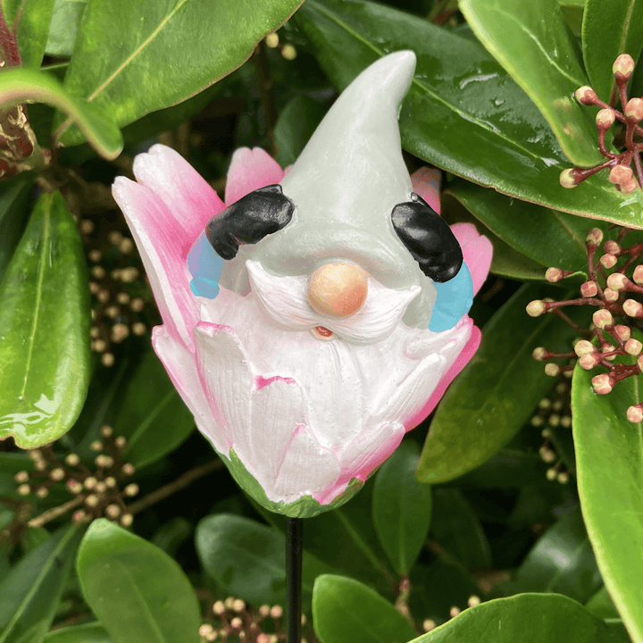 gnome stake with grey hat and pink flower in front of outdoor foliage